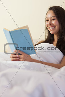 Pretty young asian woman sitting in bed reading a book