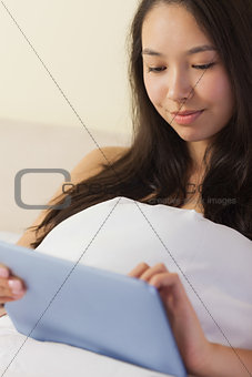 Pretty young asian woman sitting in bed using her digital tablet