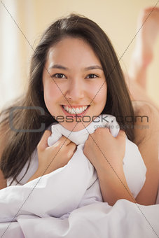 Cute young asian woman holding her duvet smiling at camera