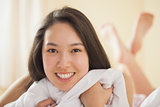 Cute young asian woman grasping her duvet and smiling
