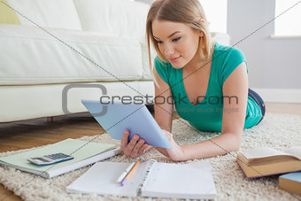 Attractive woman lying on floor using tablet to do her homework
