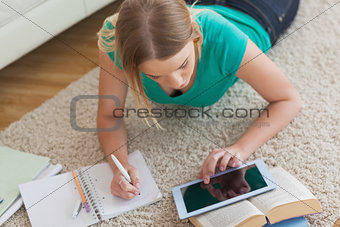 Blonde woman lying on floor using tablet to do her assignment