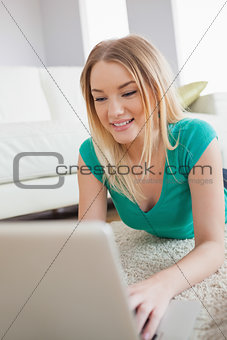 Happy woman lying on floor using laptop
