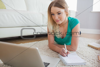 Smiling blonde lying on floor doing her homework using laptop