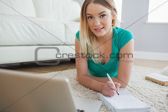 Happy blonde lying on floor doing her assigment using laptop