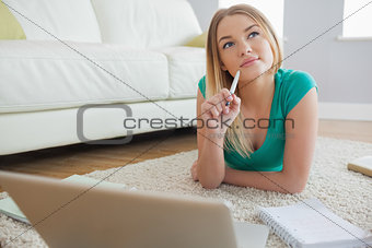 Thoughtful blonde lying on floor doing her assigment using laptop