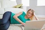 Smiling woman lying on floor using laptop
