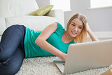 Happy woman lying on floor looking at laptop screen
