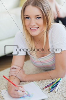 Smiling woman lying on floor sketching on paper