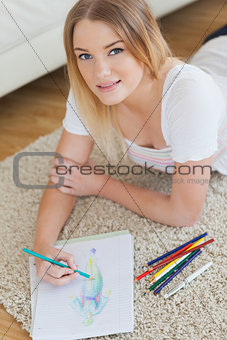 Smiling young woman lying on floor sketching on paper