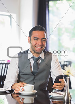 Smiling businessman having coffee and holding phone