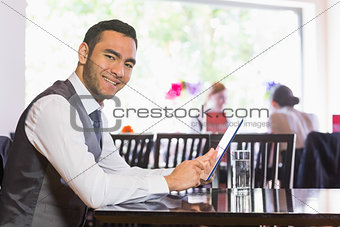 Happy businessman using tablet and smiling at camera