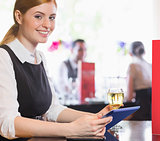 Attractive businesswoman holding tablet and wine glass and smiling at camera