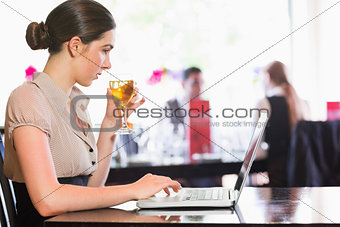 Attractive businesswoman holding wine glass while working on laptop