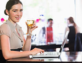 Happy businesswoman holding wine glass using laptop and looking at camera