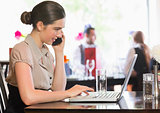 Businesswoman working on laptop while calling on phone