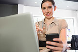Smiling businesswoman holding glass of water and phone in a cafe