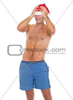 Smiling man in beach shorts pulling santa hat over eyes