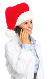 Happy doctor woman in santa hat talking mobile phone