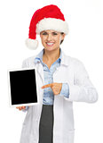 Happy doctor woman in santa hat pointing on tablet pc blank scre