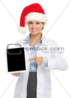 Happy doctor woman in santa hat pointing on tablet pc blank scre