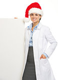 Happy doctor woman in santa hat showing blank billboard
