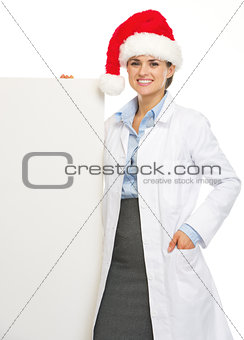 Happy doctor woman in santa hat showing blank billboard