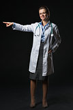 Full length portrait of smiling doctor woman pointing on copy sp