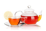 Glass cup with lemon slice and teapot of black tea