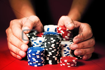 Man's hands move the winnings casino chips on red table.