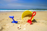 Child's beach bucket and spade on a sandy beach with seashells