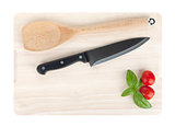 Cooking utensils and tomato with basil over cutting board