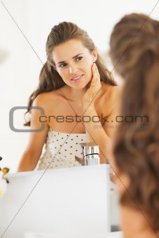 Happy young woman checking facial skin condition in bathroom