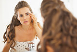 Concerned woman checking facial skin condition in bathroom