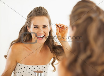 Happy young woman with tweezers in bathroom