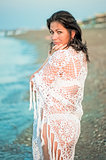 Portrait of a beautiful girl in a white shawl on the beach.