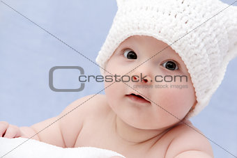 baby in white hat lies on bed