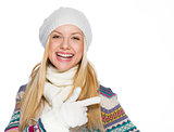 Smiling girl in winter clothes pointing on copy space