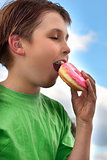 Boy biting a yummy pink iced doughnut (donut)