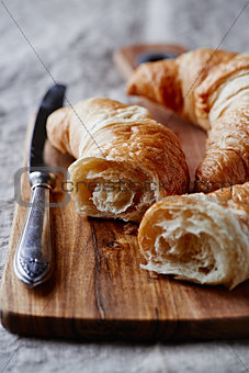 Croissant and a table knife on wooden chopping board