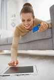 Happy young woman with credit card using tablet pc while laying 