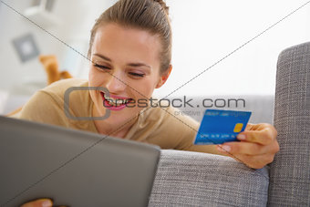 Smiling young woman with credit card using tablet pc while layin