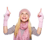 Smiling girl in winter clothes pointing up on copy space