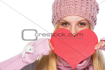Happy girl in winter clothes hiding behind heart shaped valentin