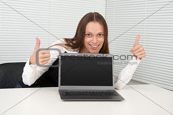 Cheerful businesswoman showing thumbs up in front of laptop
