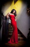 The beautiful girl in a long red dress posing in a vintage scene.Young beautiful woman wearing a red dress in the old hotel.Sensual elegant young woman in red dress and indoor shot.