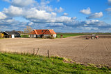 tractor plowing field by farmhouse