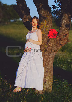 Young cute pregnant woman wearing white dress in decorated garde