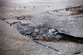 Broken pavement and pothole asphalt road after winter.