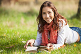 Beautiful young girl reading book while lying on grass